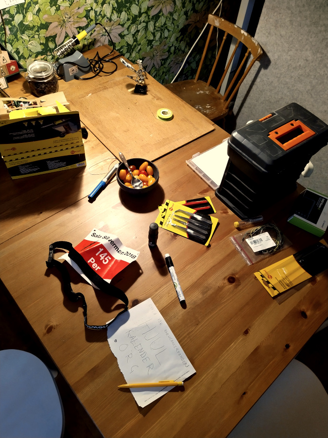 Bord med nummerlapp och pennor samt elektronik och lödkolv i bakgrunden